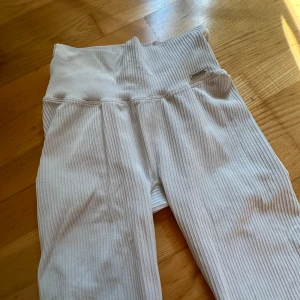 Vita ribbade leggings från Aim'n - Säljer ett par vita ribbade leggings från Aim'n med hög midja och stretchigt material. De har en snygg, tight passform och diskret Aim'n-logga i metall framtill. Perfekta för chill eller träning och superbekväma att bära hela dagen. Lite lätt smuts på bakbenen (går säkert bort med diskmedel eller galltvål)