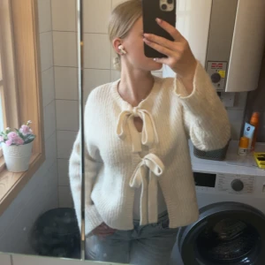 Vit stickad kofta med knyt från Gina Tricot - Supermysig vit stickad kofta från Gina Tricot i storlek XS. Koftan har två stora knytband framtill och är ribbstickad med lång ärm. Perfekt att slänga på sig över en topp för en chill och trendig look.
