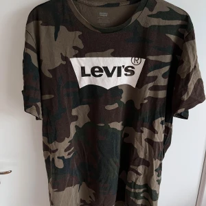 Levi's camo t-shirt med logga - Strl XL - Camo t-shirt från Levi's i storlek XL. Klassisk rund halsringning och korta ärmar. T-shirten är i ett fint skick med tecken på andvändning då trycket på bröstet men i övrigt hel och ren. 