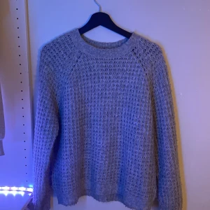 Grå stickad tröja med grovt mönster - Säljer en mysig grå stickad tröja med grovt hålmönster. Tröjan har rund hals och långa ärmar, perfekt för att hålla sig varm under kyliga dagar. Den har en loose passform och är superenkel att matcha med jeans eller mjukisbyxor.