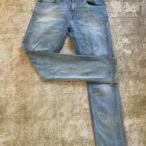 Ljusblå jeans från Tiger of Sweden - Säljer ett par snygga ljusblå jeans från Tiger of Sweden. Klassisk femficksmodell med raka ben och normal passform. Jeansen har snygga slitningar och detaljer som bruna sömmar och läderpatch bak i midjan. Perfekta till en avslappnad stil.