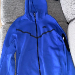 Blå Nike Tech kofta - Säljer en blå nike tech kofta i storlek S. Den är lite norpig precis bredvid dragkedjan därav lägre pris