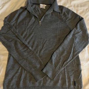 Grå half zip tröja från Calvin Klein - Snygg grå långärmad tröja från Calvin Klein med half zip-dragkedja och krage. Tröjan är stickad i mjukt material och har en clean, stilren look som passar perfekt till jeans. Klassisk passform och diskret logga vid nederkanten. Storlek S och inga defekter 