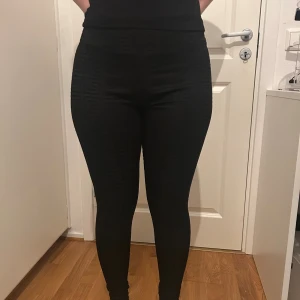 Svarta leggings från Amisu med mönster - Svarta leggings från Amisu i storlek M med diskret geometriskt mönster i tyget. De är högmidjade och har en tight passform som sitter snyggt längs benen. Materialet är stretchigt och består av polyester och elastan, vilket gör dem bekväma och följsamma.