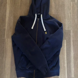 Polo Ralph lauren zip hoodie - Säljer en Polo Ralph lauren hoodie i färgen marinblå i nästan nyskick. Nypriset ligger runt 2000kr och vid fler frågor och funderingar kontakta gärna säljaren!
