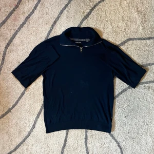 Marinblå half zip tröja Jack & Jones - Säljer en marinblå tröja från Jack & Jones med kort ärm och half zip-dragkedja vid kragen. Tröjan har en klassisk och stilren look, perfekt till jeans eller chinos. Materialet är mjukt och bekvämt, passar både till skolan och häng med vänner.