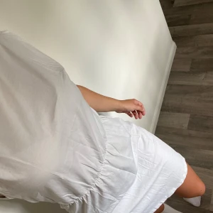 Vit kort klänning från hm  - Säljer en vit kort klänning från hm med rund hals och ärmlös design. Klänningen har en markerad midja med resår som ger en snygg siluett. Tillverkad i mjuk bomull, perfekt för varma dagar. Enkel och clean look som är lätt att styla.