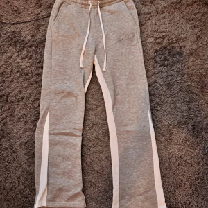 Flared Grå mjukisbyxor  - Snygga Flared grå mjukisbyxor längs benen och elastisk midja med snörning. Byxorna har fickor fram och en stor M-logga bak. Perfekta för chill eller träning, riktigt sköna och stilrena.