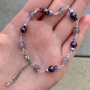Lila pärlarmband med silverkedja - Unikt armband med lila och mörklila pärlor i olika storlekar, trätt på en tunn silverfärgad kedja med justerbar kedja och lås. Pärlorna har en cool glans och ger ett snyggt, trendigt intryck. Perfekt för dig som gillar färg och vill sticka ut lite extra.