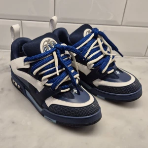 Louis Vuitton skates - Exklusiva Louis Vuitton sneakers i marinblått och vitt med grova blå och vita snören. Skorna har detaljer i skinn och mesh, samt ikoniska LV-blommor på hälen och sulan. Snygg, sportig design med rund tå och platt sula. Perfekta för dig som gillar statement pieces. Strl 42 1/2 till 43 1/2. Pris kan diskuteras vid snabbt köp.