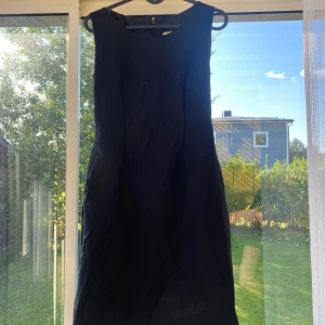 Svart ärmlös klänning - Snygg svart klänning med enkel och stilren design. Klänningen är ärmlös och har en rundad halsringning. Passformen är normal och längden går till knäna. Perfekt för dig som gillar minimalistisk stil och vill ha en klassisk look.