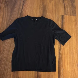 Marinblå kortärmad tröja - En stilren svart tröja med korta ärmar och rund hals. Tröjan har ribbade detaljer vid ärmslut och nederkant, vilket ger en snygg och enkel look. Perfekt att matcha med jeans eller kjol för en clean vibe.