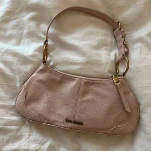 Vintage steve madden väska - Säljer en snygg ros axelväska från Steve Madden med guldiga metalldetaljer och justerbart axelband. Väskan är även vintage