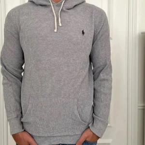 Grå hoodie från Ralph Lauren - Säljer en stilren grå hoodie från Ralph Lauren med en liten broderad logga på bröstet. Tröjan har en känguruficka och justerbar huva med snören. Perfekt för en avslappnad look. Tröjan passar även M! Skicket är också bra förutom de lilla hållet på sista bilden. 