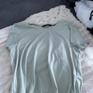 Ljusgrön ribbad topp från Vero Moda - Superfin ljusgrön ribbad topp från Vero Moda med korta ärmar och volangdetalj vid ärmslut. Tunt och mjukt material som känns skönt mot huden. Perfekt till jeans eller kjol för en chill look.