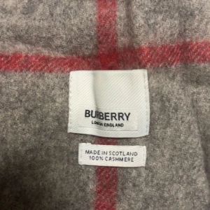 Rutig grå halsduk från Burberry - Snygg halsduk från Burberry i klassiskt rutigt mönster med grå bas och inslag av svart, vitt och rött. Tillverkad i 100% kashmir för extra mjuk och lyxig känsla. Perfekt accessoar för att lyfta din outfit med ikonisk stil.