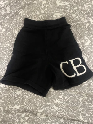 CB shorts - Säljer ett par svarta stickade shorts med hög midja och två bakfickor. På ena benet finns en stor vit CB-detalj som ger en cool touch. Perfekta för sommarens avslappnade dagar eller när du vill chilla hemma.