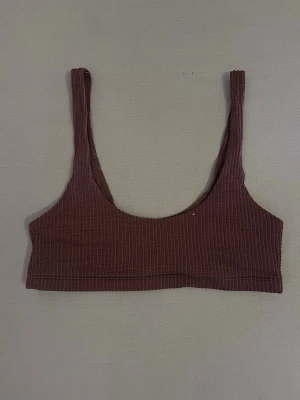 BH - Säljer en brun ribbad bralette med breda axelband och utan vaddering. Bh:n har en enkel, sportig design och är tillverkad i ett stretchigt, mjukt material som ger en bekväm känsla. Perfekt för dig som gillar minimalistisk stil.