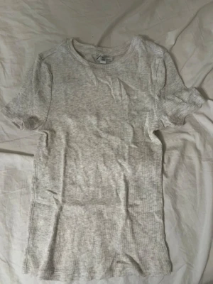 Ljusgrå ribbad t-shirt  - En enkel och stilren ljusgrå t-shirt, ribbad, har rund halsringning och korta ärmar.