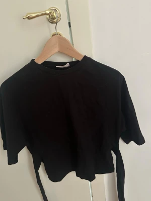 Svart topp med öppen rygg - Säljer en svart topp med korta ärmar och öppen rygg. Denna tidigare virala Nelly toppen. Perfekt till höga jeans eller kjol. Enkel och stilren design som passar till mycket. Materialet känns mjukt och bekvämt. 