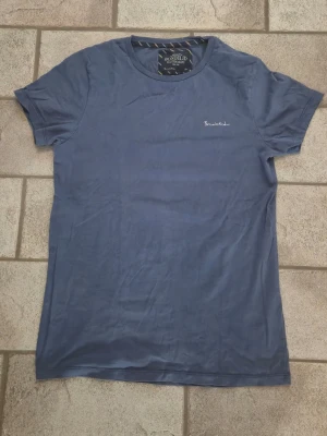 Blå t-shirt från Bondelid - Snygg blå t-shirt från Bondelid med diskret broderad logga på bröstet. Klassisk rund halsringning och korta ärmar. Tillverkad i mjuk bomull som känns skön mot huden. Perfekt till jeans eller shorts för en avslappnad look.