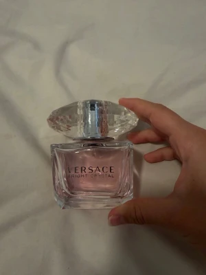 Versace Bright Crystal parfym - Versace Bright Crystal parfym i en lyxig glasflaska med ljusrosa doft och en stor, kristalliknande transparent kork. En blommig doft med fruktiga inslag. Den friska och strålande doften inleder med fräsch yuzu och noter av saftigt granatäpple för att sen övergå i ett vackert hjärta av pioner och mjuk magnolia
