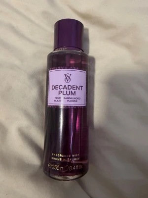 Decadent Plum Fragrance Mist - En lyxig body mist från Victoria's Secret i doften Decadent Plum. Flaskan är lila med ett matchande lock och rymmer 250 ml. Doften har inslag av plommon, sandelträ och blommiga toner. Perfekt för dig som gillar fruktiga och sensuella dofter.
