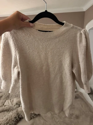 Beige stickad tröja - Säljer en beige stickad tröja med puffärmar och rund halsringning. Tröjan har ribbade muddar vid ärmslut och nederkant samt en mjuk, mysig struktur. Perfekt för dig som gillar en enkel men trendig look.