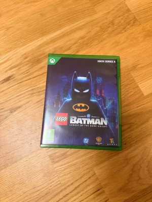 LEGO Batman Xbox Series X spel - Säljer LEGO Batman: Legacy of the Dark Knight till Xbox Series X. Omslaget är svart och grönt med Batman i LEGO-format på framsidan och coola Gotham City-detaljer i bakgrunden. Perfekt för dig som gillar action, äventyr och LEGO-spel.
