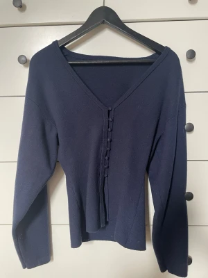 Mörkblå kofta med knappar från gina tricot - Mörkblå kofta med v-ringning och dekorativa tygklädda knappar framtill. Långärmad och figurnära modell i mjukt stickat material. Perfekt för lager-på-lager och enkel att styla till olika outfits. 
