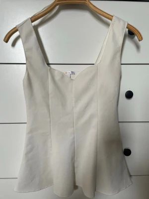 vit peplumtop från gina 💕 - Snygg vit peplumtop med breda axelband och lätt utsvängd nederkant. Toppen har en söt v-ringning framtill och är ärmlös, perfekt för varma dagar. Enkel och stilren design som passar till det mesta. Har en liten missfärgning på kanten på baksidan :)!!
