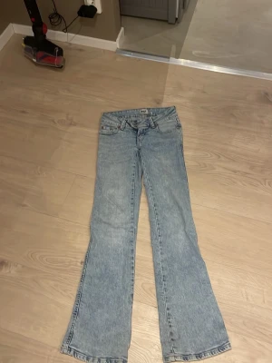 Ljusblå bootcut jeans med dubbla knappar - Säljer ett par ljusblå bootcut jeans med dubbla knappar i midjan och klassisk femficksdesign. Jeansen har en snygg tvättad look och är tillverkade i denim. Perfekta för dig som gillar retrostil och vill ha ett par jeans som sticker ut.