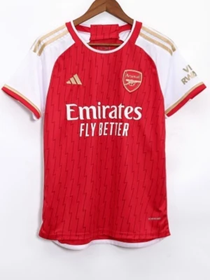 Arsenal matchtröja röd/vit - Snygg Arsenal matchtröja i rött och vitt med gulddetaljer och klubbmärke på bröstet. Tröjan har korta ärmar, rund hals och Adidas-logga. Tillverkad i lätt och ventilerande funktionsmaterial, perfekt för fotbollsträning eller match.