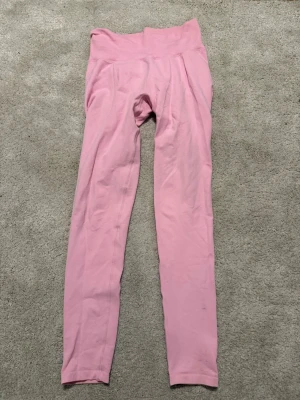 Rosa seamless leggings från Aim'n - Säljer ett par ljusrosa seamless leggings från Aim'n med hög midja och ribbad linning. Materialet är stretchigt och mjukt, perfekt för träning eller chill. Tight passform som framhäver benen och ger en snygg siluett.