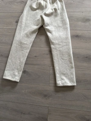 Grå mjukisbyxor från Essentials - Säljer ett par ljusgrå mjukisbyxor från Essentials. Byxorna har resår i midjan och raka ben, perfekta för chill dagar. Tillverkade i mjukt och skönt material som känns riktigt bekvämt. Passar dig som gillar en clean och enkel stil.