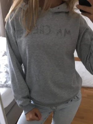Grå hoodie med strassdetaljer - Säljer en ljusgrå hoodie med huva och strassdetaljer på bröstet som bildar text. Hoodien har en avslappnad passform och är tillverkad i mjukt sweatshirtmaterial. Perfekt för en chill och casual look. Ganska sliten som ni ser på andra bilden