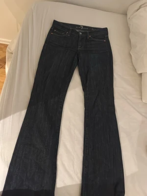 Mörkblå bootcut jeans - Snygga mörkblå jeans med bootcut-modell och klassisk femficksdesign. Jeansen har kontrastsömmar och kopparfärgade nitar. Perfekta för dig som gillar en tidlös och avslappnad stil. Materialet är denim i bomull.