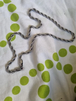 Tjockt tvinnat silverfärgat halsband - Säljer ett stilrent halsband i silverfärgad metall med tvinnad kedja. Halsbandet har en robust känsla och ett klassiskt repmönster som ger en cool touch till din outfit. Perfekt för dig som gillar chunky smycken och vill sticka ut lite extra.