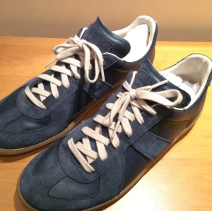 Navy Gats maison marginela  - Stilrena mörkblå sneakers med beige snören och gummisula. Ovandelen är i en mix av mocka och slätt läder, vilket ger en snygg kontrast. Insidan är vit och skon har en klassisk låg silhuett som passar till många olika stilar. Skriv vid intresse billigare vid snabb affär.