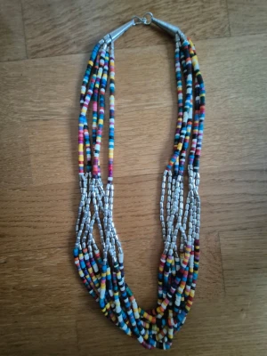 Flerfärgat pärlhalsband i flera rader - Unikt halsband med flera rader små pärlor i olika färger som blått, gult, rosa, vitt och svart. Halsbandet har även inslag av silverfärgade pärlor och ett metallspänne. Perfekt för dig som vill ha en färgklick till din outfit. Ny/ oanvänd vintage 