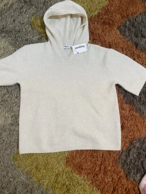 Beige hoodie från Kappahl med huva - Mjuk och stilren beige hoodie från Kappahl i storlek 170. Tillverkad av 65% återvunnen polyester. Hoodien har korta ärmar, ribbade muddar och en klassisk huva. Perfekt för en avslappnad och trendig look.
