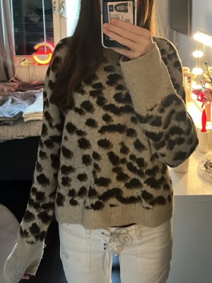 Beige leopardmönstrad stickad tröja - Snygg stickad tröja i beige med leopardmönster i svart och brunt. Tröjan har rund halsringning, långa ärmar och ribbade muddar vid ärmslut och nederkant. Ser ut som ny! 💓
