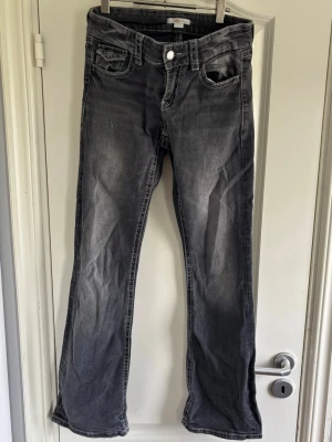 Grå bootcut jeans med slitningar - Säljer ett par grå bootcut jeans med snygga slitningar och tvättade detaljer. Jeansen har klassisk femficksmodell, normal midja och raka ben som går ut lite nedtill. Perfekta för en avslappnad och trendig look.