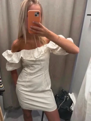 Vit offshoulder kortklänning - Snygg cream vit kortklänning med offshoulder och volangdetalj upptill. Klänningen har en figurnära passform och är perfekt för sommarens alla tillfällen. Tillverkade i ett linne material som känns bekvämt mot huden.
