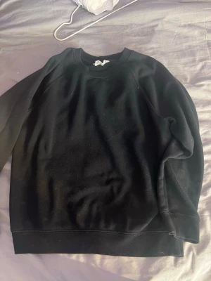 Svart basic sweatshirt - En enkel svart sweatshirt med rund hals och ribbade muddar vid ärmar och nederkant. Perfekt till jeans eller mjukisbyxor. Klassisk modell utan tryck eller mönster, tillverkad i mjukt material.