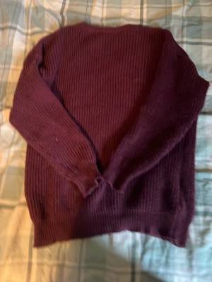 Mörklila ribbstickad tröja - Mysig mörklila stickad tröja med ribbad struktur och långa ärmar. Perfekt för lager på lager och enkel att matcha med jeans eller kjol. Tröjan har rund halsringning och mjukt material som känns skönt mot huden.