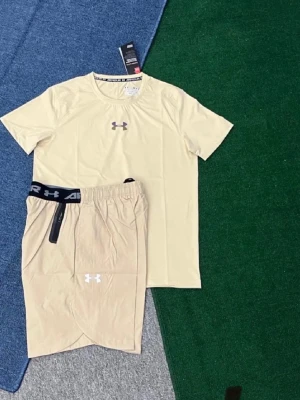 Beige träningsset från Under Armour - Snyggt beige träningsset från Under Armour med t-shirt och matchande shorts. T-shirten har rund hals och logga på bröstet, shortsen har elastisk midja och logga på benet. Perfekt för gymmet eller löprundan.