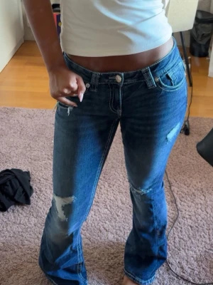 Blå bootcut jeans med slitningar från GinaTricot  - Säljer ett par mörkblå bootcut jeans med slitna detaljer på låren och knäna. Jeansen har låg midja, klassisk femficksmodell och är tillverkade i denim. Perfekta för dig som gillar en avslappnad och trendig stil. De är från Gina. Och används max 2 gånger. 