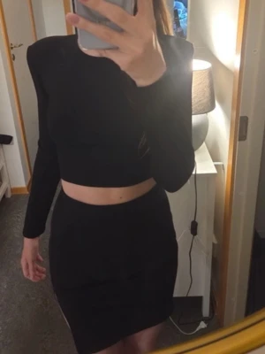 Nelly set – crop top & minikjol (top and skirt) - Pris kan diskuteras! Säljer detta otroligt snygga och matchande tvådelade set i svart! Perfekt till både fest/utekväll, uppklädda tillfällen eller om man bara vill känna sig lite extra fin.✨️  🖤 Innehåller:   - Långärmad crop top med vadderade axlar och tight passform. - Matchande högmidjad minikjol med slits i sidan för en extra snygg detalj. (slutar över knät) Skriv gärna vid frågor 🫶