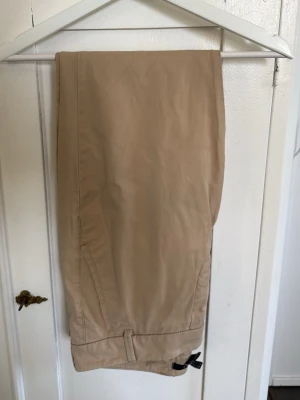 Beige chinos från GANT - Snygga beige chinos från GANT i klassisk rak modell. Tillverkade i ett mjukt och slitstarkt bomullstyg med diskreta fickor och justerbar detalj vid benslutet. Perfekta för en clean och stilren look. Skriv om ni har några frågor! 